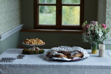 Ekmek, çiçekler, çatallar, mutfak masasında bir mum. Pencere içeri 