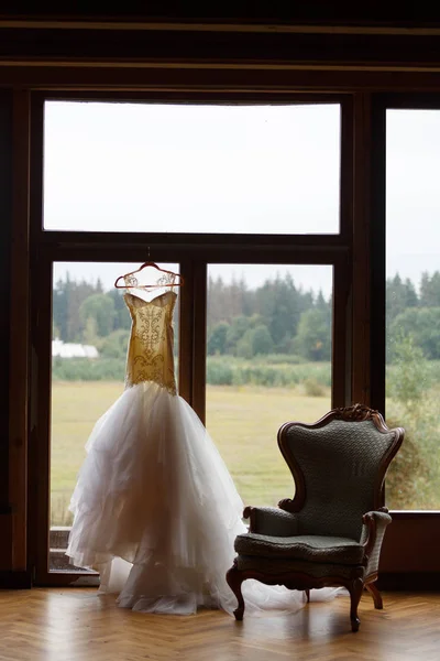 Bröllopsklänningen hänger på fönstret, bredvid den finns en chai — Stockfoto