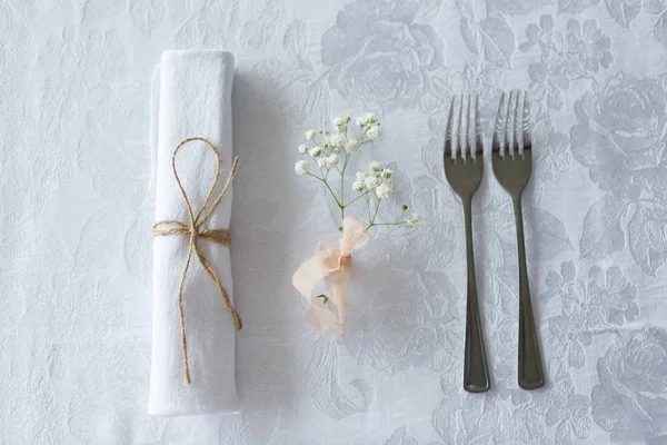 Салфетка, цветок и две столовые вилки на белом покрывале — стоковое фото