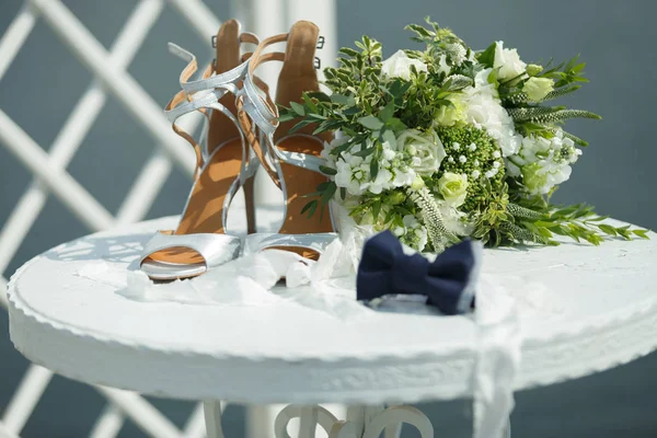 Acessórios de casamento em uma mesa branca: um buquê de noivas, sapatos e um laço de noivos — Fotografia de Stock
