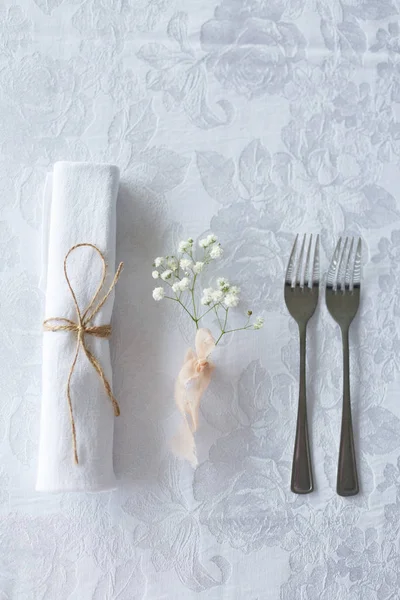 Салфетка, цветок и две столовые вилки на белом покрывале — стоковое фото