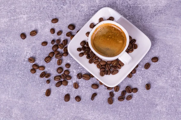 Varmt kaffe i en kopp, kaffebönor är utspridda i närheten. Visa oss — Stockfoto