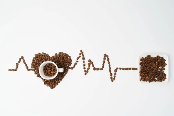 A cup and bun with coffee beans, a cardiogram laid out from coff — Stock Photo, Image