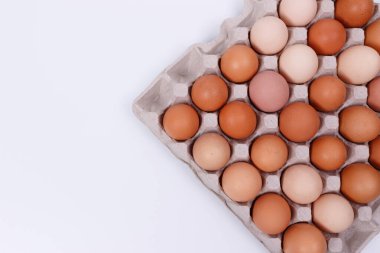 Kağıt bir kabın içinde sarı, bej ve beyaz tavuk yumurtaları. İzole et