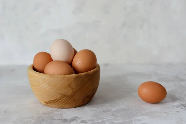 Chicken eggs in a wooden plate, one egg lies on the side. Close-up. Side view