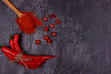 Tam ve dilimlenmiş kırmızı biber kabukları, kırmızı biberli ahşap kaşık. Üst Manzara, kapat. Koyu arkaplan