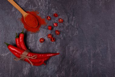 Tam ve dilimlenmiş kırmızı biber kabukları, kırmızı biberli ahşap kaşık. Üst Manzara, kapat. Koyu arkaplan