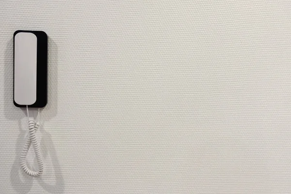 Dairenin duvarında dahili telefon var. Sol tarafta yer alıyor. Yakın plan. Hafif duvar kağıdı dokusu