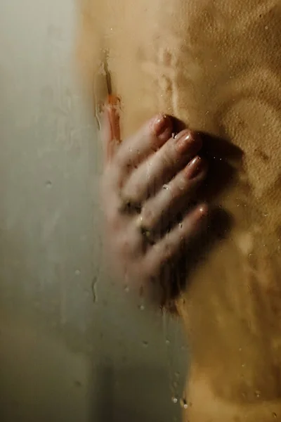 A woman hugs a man in the shower. Womans hand on the mans back. Behind the misted glass. black and white photography