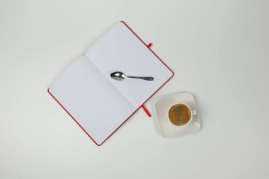 Beyaz arka planda bir fincan kahve, defter ve kaşık. Yakın plan. Yukarıdan görüntüle.