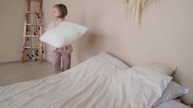 Kız yatağı yapıyor, yastıkları katlıyor. Yan görünüm