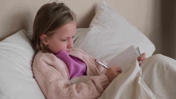 这个女孩躺在床上用毯子盖住 然后在笔记本上写字 侧视图 — 图库视频影像