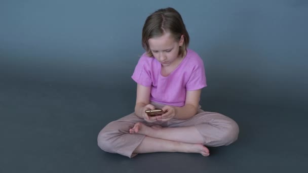 Una Chica Sienta Suelo Juega Con Teléfono Móvil Fondo Gris — Vídeo de stock