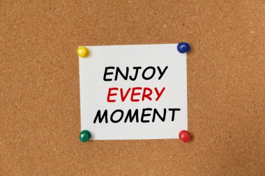 Bir mantar panoya yapıştırılmış bir çıkartma üzerine her an yazılan metin ENJOY