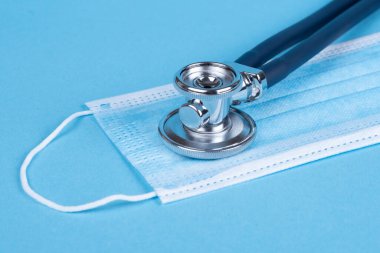 Koronavirüs 19 'u kapsıyor. Kirlenmeye, virüslere, gribe ve koronavirüse karşı yüz maskesi. Mavi tıbbi maske, mavi steteskop ve mavi arka plan. Sağlık ve Cerrahi Konsept.