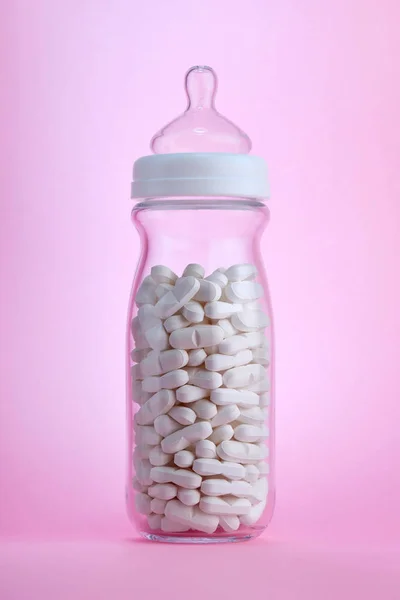 Baby bottle containing white pills on pink background — Stock Photo, Image