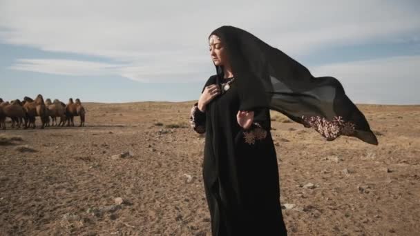 Красивая женщина национальная черная одежда, Абая гуляет степные верблюды, пустыня, медленно — стоковое видео