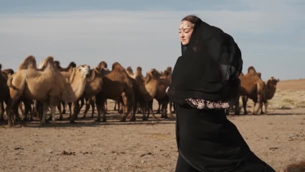 Vacker kvinna nationella svarta kläder, abaya, promenader stäpp kameler, öken, långsamt — Stockvideo