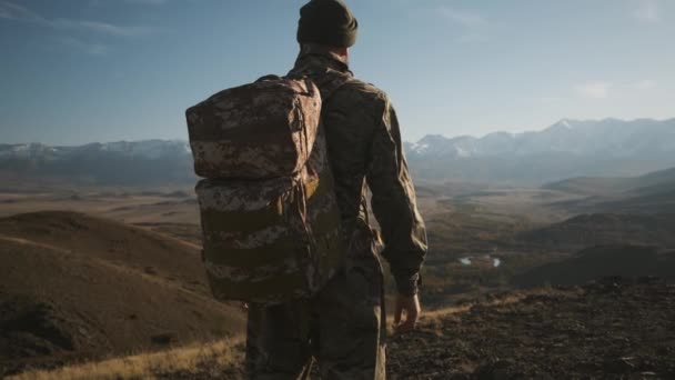 Male traveler beard military suit backpack, looks snow-capped mountains — Stock Video