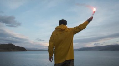 Sarı yağmurluk, el sallayan sinyal ışığı, göl dağlarının kenarındaki uçurum. Gezgin.
