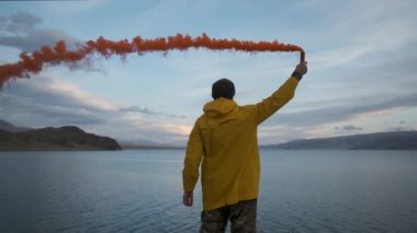 Sarı yağmurluk, el sallayan sinyal ışığı, göl dağlarının kenarındaki uçurum. Gezgin.