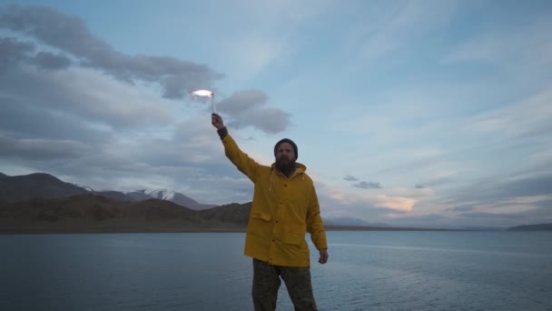 Άνθρωπος κίτρινο αδιάβροχο, κυματίζει φως σήμα, άκρη γκρεμό κοντά σε βουνά λίμνης.ταξιδιώτη — Αρχείο Βίντεο