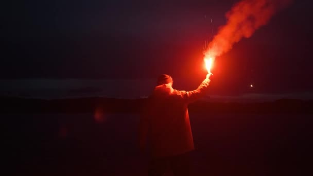 Man regenjas, zwaaiend rood rooksignaal, licht, meer bergen.reiziger nacht — Stockvideo