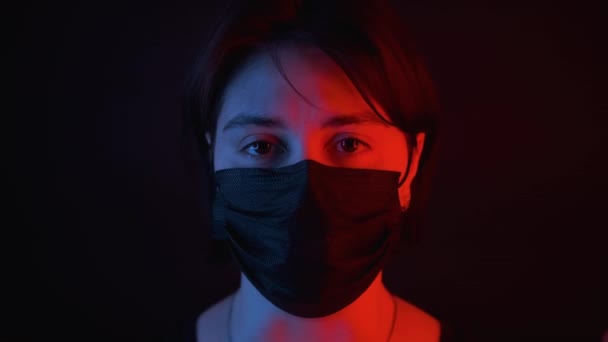 Blank meisje hoesten in zwart medisch masker, rood en blauw neon licht op gezicht — Stockvideo