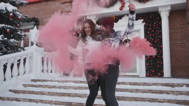 Junges Paar zu Weihnachten, Silvester spielen rosa Rauchgranate in der Nähe geschmückten Hauses — Stockvideo