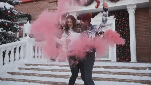 Jovem casal no Natal, ano novo jogar granada de fumaça rosa perto da casa decorada — Vídeo de Stock