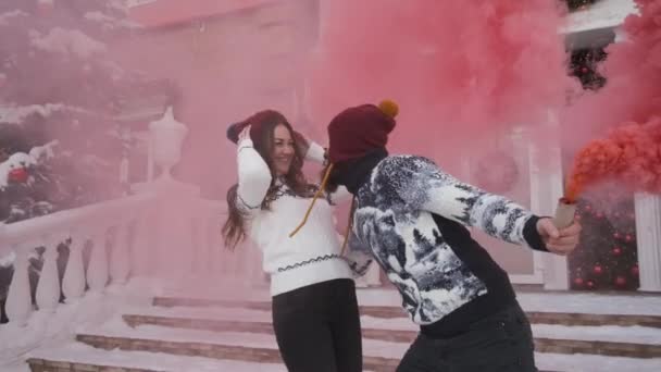 Young couple at Christmas,new year play pink smoke grenade near decorated house — Stock Video