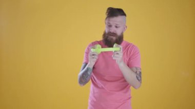 Pembe tişörtlü adam sarı arka planda müzik ve kulaklık dinliyor.