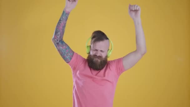 Hombre de camiseta rosa escuchando música y auriculares, sobre fondo amarillo — Vídeos de Stock