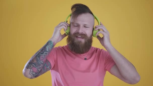 Hombre de camiseta rosa escuchando música y auriculares, sobre fondo amarillo — Vídeos de Stock