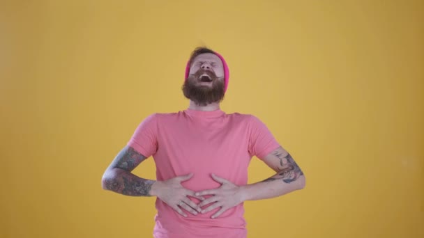Caucásico hombre ríe, sostiene su estómago, fondo amarillo, de cerca — Vídeos de Stock