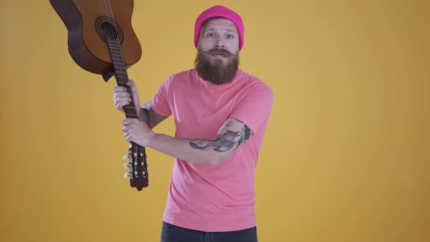 Hombre caucásico agitando la guitarra, gritando, muestra agresión, fondo amarillo — Vídeos de Stock