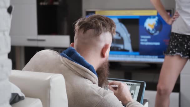 Hombre trabaja en casa, se basa en cuarentena tableta frente a la televisión con noticias — Vídeo de stock