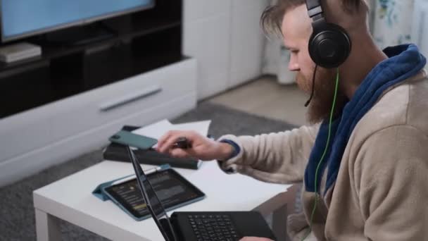 Hombre trabaja en casa en auriculares en cuarentena de la epidemia mundial de coronavirus — Vídeo de stock