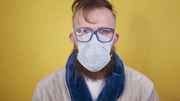 Man in housecoat met haveloos kapsel zet op medisch masker op gele achtergrond — Stockvideo