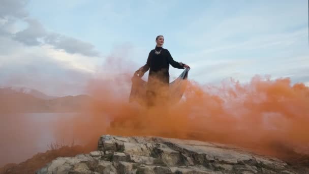 Kvinna i svart klänning står på kanten av klippan pittoreska, signal eld, röd rök — Stockvideo