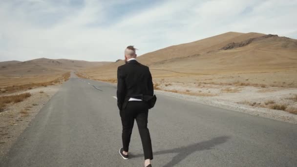 Homme caucasien employé de bureau s'éloigne le long d'une route de montagne pittoresque vide — Video