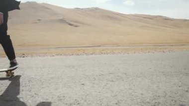 Siyah takım elbiseli adam ıssız çöl yolunda yürüyor dağlarda kaykayla