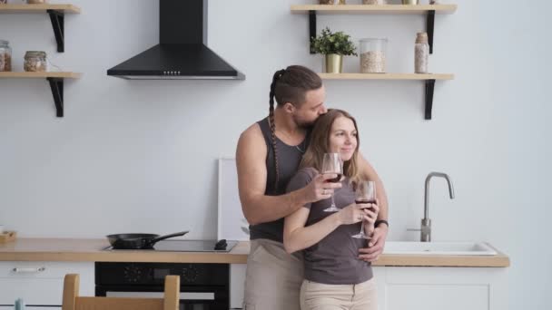 Joven feliz pareja familiar activa en la cocina moderna, sonriendo beber vino tinto — Vídeos de Stock