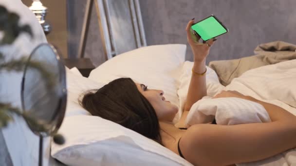 Belle fille est couché dans le lit à la maison en regardant son smartphone — Video