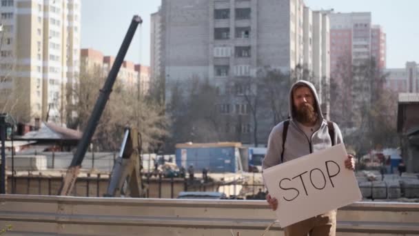 Ung man protesterar med stoppskylt, nära byggarbetsplatsen.noise och skräp — Stockvideo