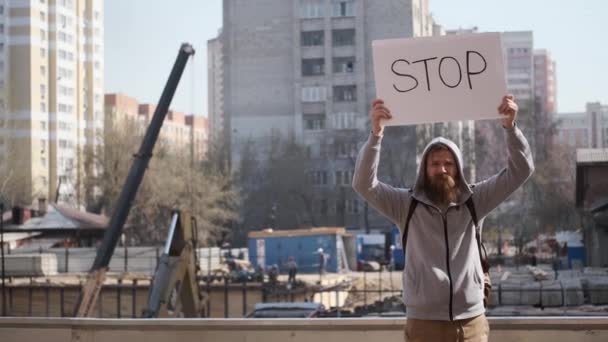 Rozzlobený mladý muž protestuje se stopkou, v blízkosti staveniště. — Stock video