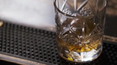 Barda cam var, buz küpleri cama düşüyor, barmen buz koyuyor ve cam alıyor.