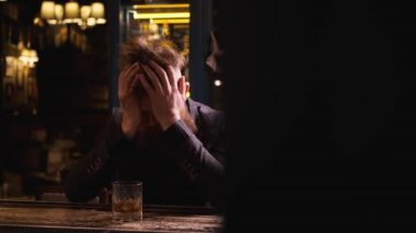 Barda bir bardak viskiyle sarhoş bir adam, kafasını tutuyor, alkol konsepti...