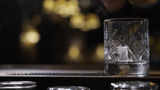 Bar há vidro, cubos de gelo caem em vidro, bartender coloca gelo e leva vidro — Vídeo de Stock