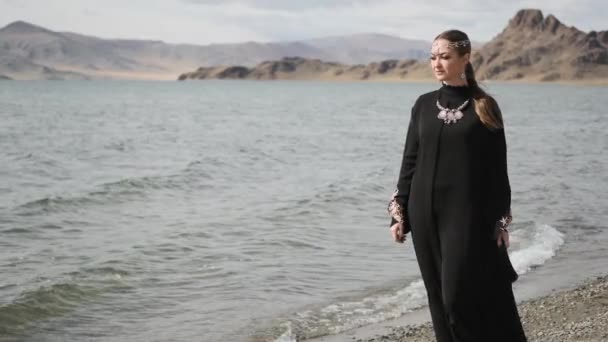 Hermosa chica camina a lo largo de las orillas de un río, cerca de grandes montañas, vestido de luto — Vídeos de Stock